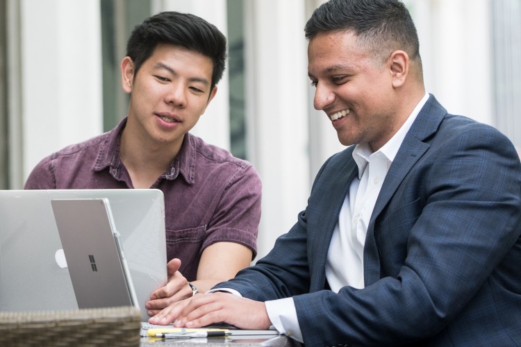 Two students share information as they work on their laptop computers